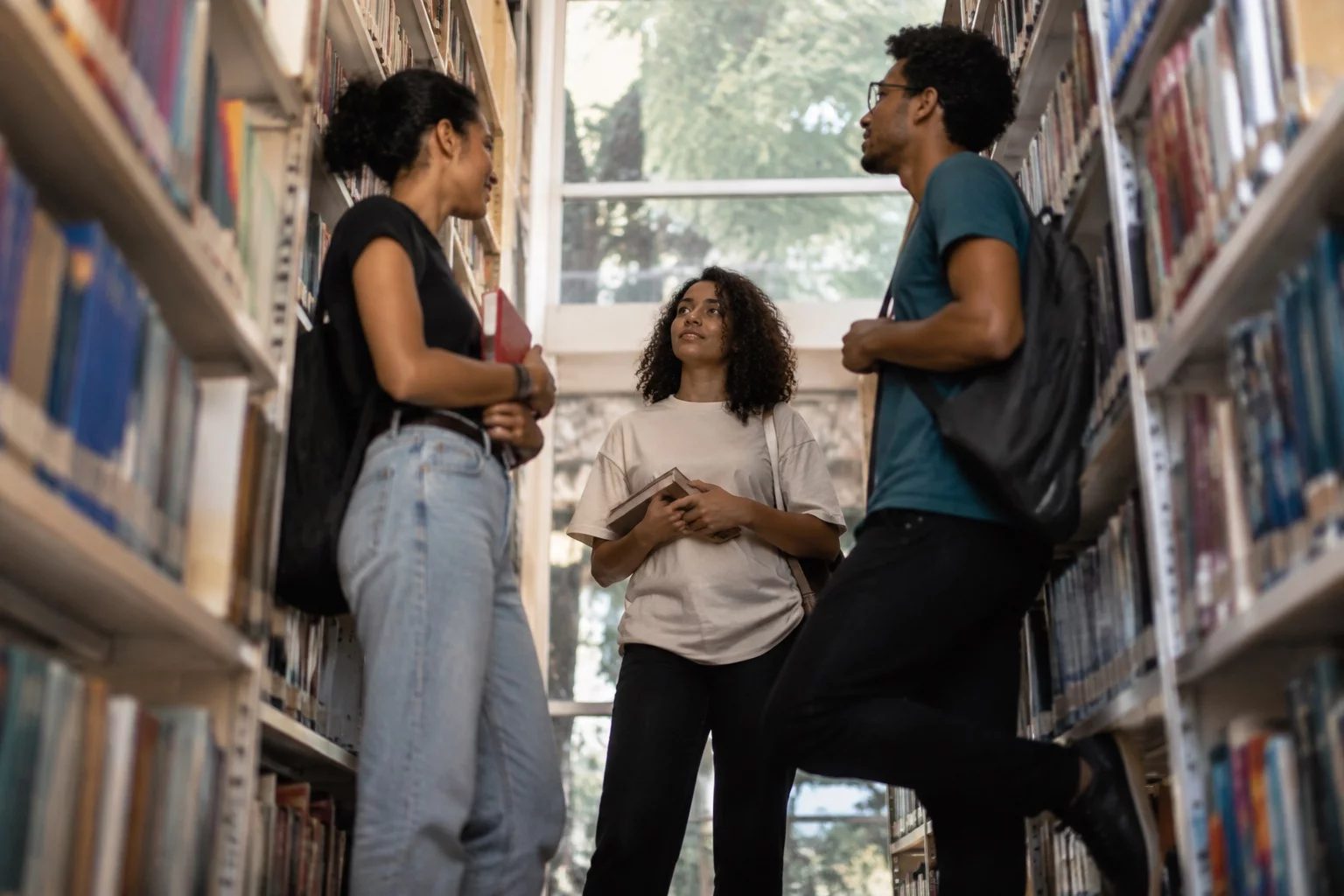 Estudantes conversando em pé entre as estantes de uma biblioteca